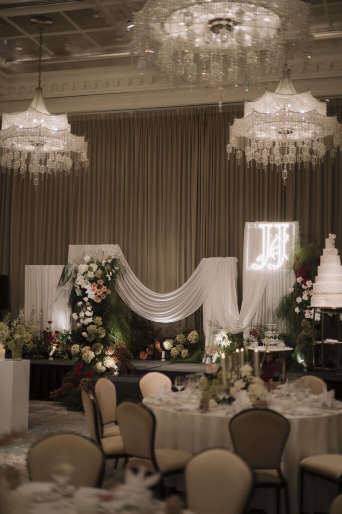 Wide reception ballroom styling with cascading drapery, floral stage arrangements, and warm ambient lighting creating a refined modern classic wedding atmosphere at Raffles Hotel Singapore