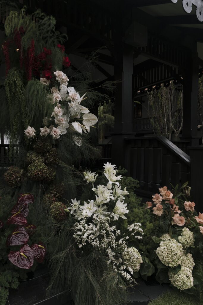 Lush ceremony floral pillar arrangement featuring cascading white florals, blush blooms, deep burgundy flowers, and textured greenery for a modern classic lawn wedding at Raffles Hotel Singapore