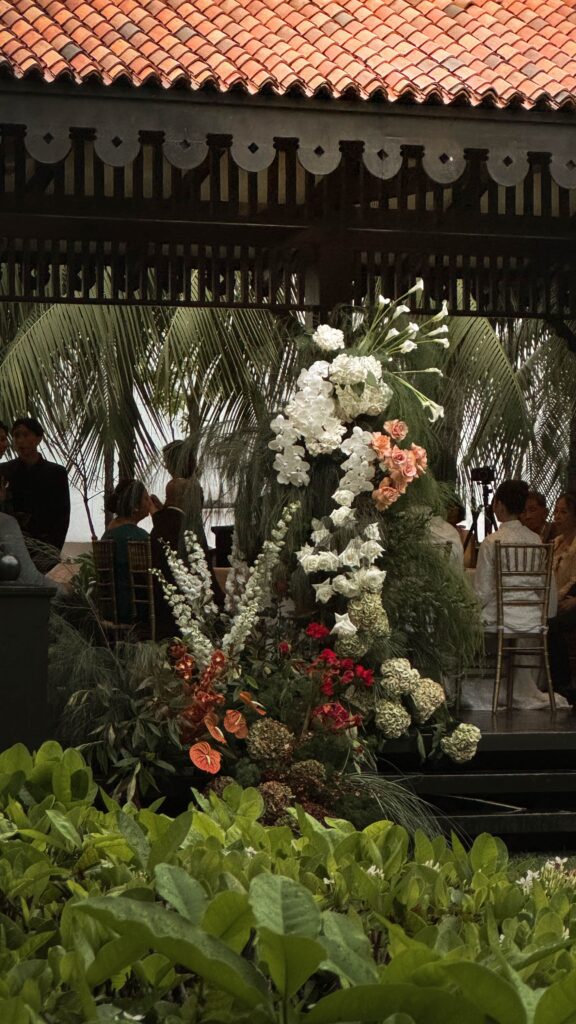 Modern classic lawn wedding floral styling with blush, ivory, and deep maroon floral arrangements framing the colonial pavilion entrance with organic garden-inspired placement at Raffles Hotel Singapore