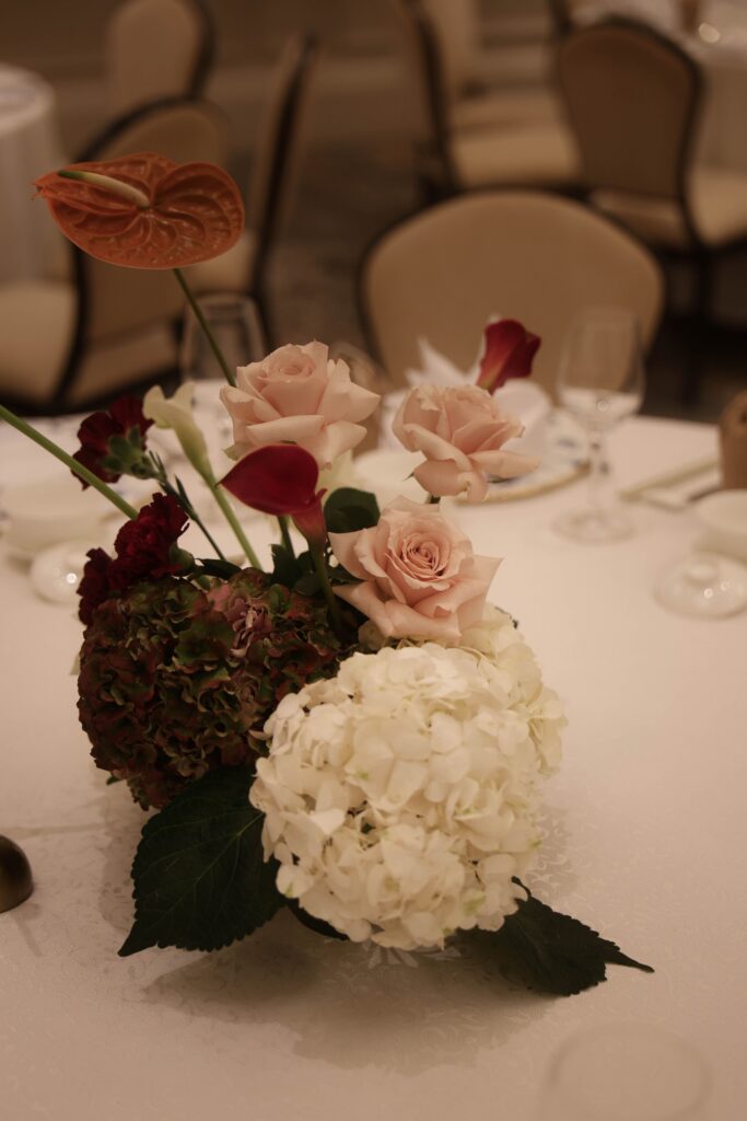 Low floral reception centrepiece with white hydrangeas, burgundy florals, blush accents, and modern classic arrangement styling for ballroom dining at Raffles Hotel Singapore