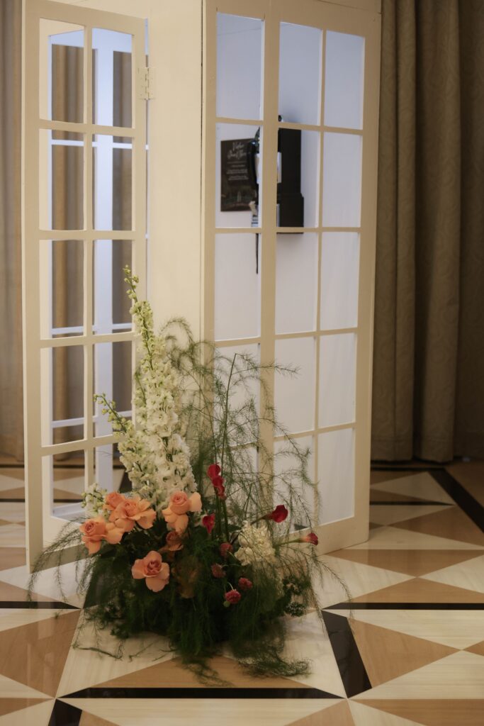Modern classic photo booth arrangement with blush and coral florals, organic greenery, and sculptural floral styling beside the reception photo booth space at Raffles Hotel Singapore
