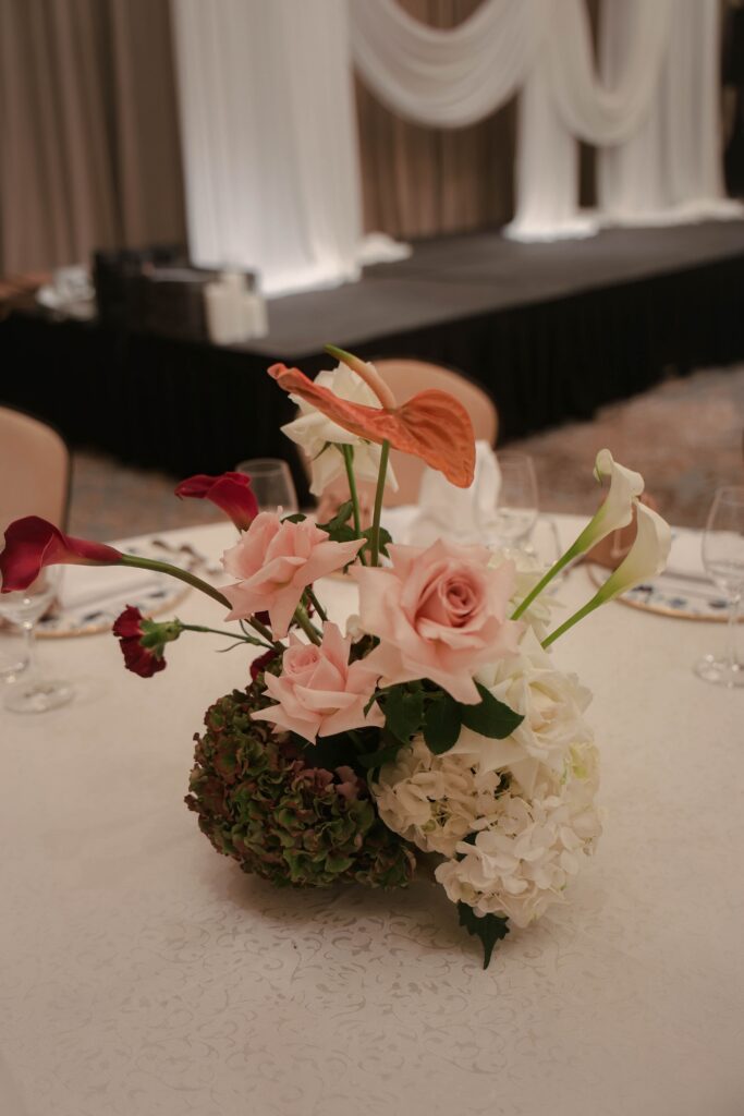 Modern classic wedding centrepiece with pink lilies, white hydrangeas, blush florals, and sculptural styling arranged for reception table decor at Raffles Hotel Singapore