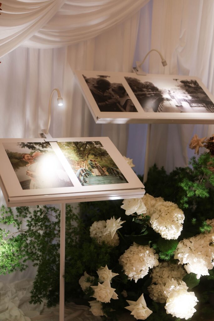 Elegant self-standing photograph display styled with soft drapery, white florals, blush roses, and organic greenery for personalised wedding styling at Raffles Hotel Singapore