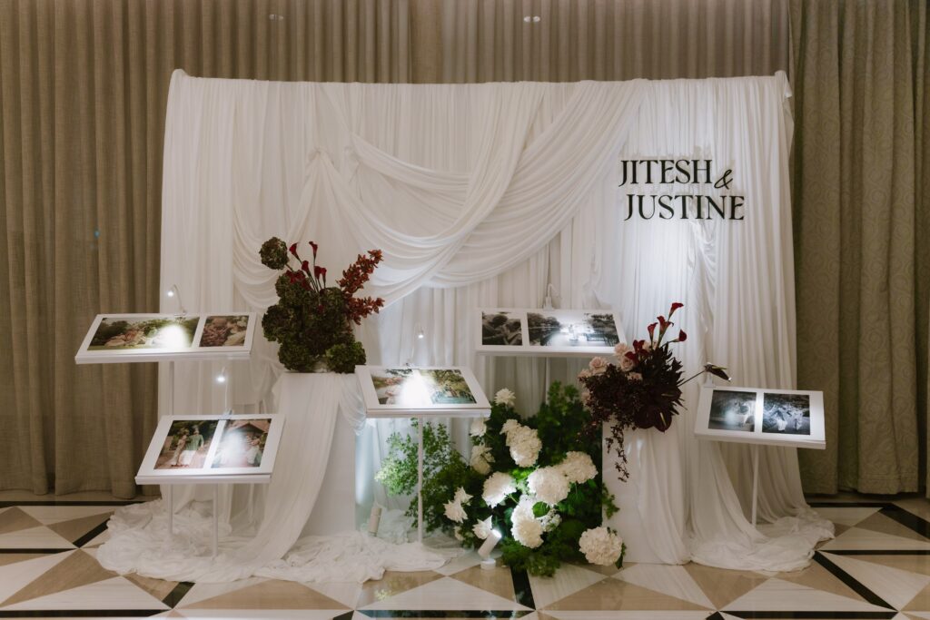 Personalised wedding styling with draped backdrop and self-standing pre-wedding photograph display framed by modern floral arrangements for a modern classic wedding reception at Raffles Hotel Singapore