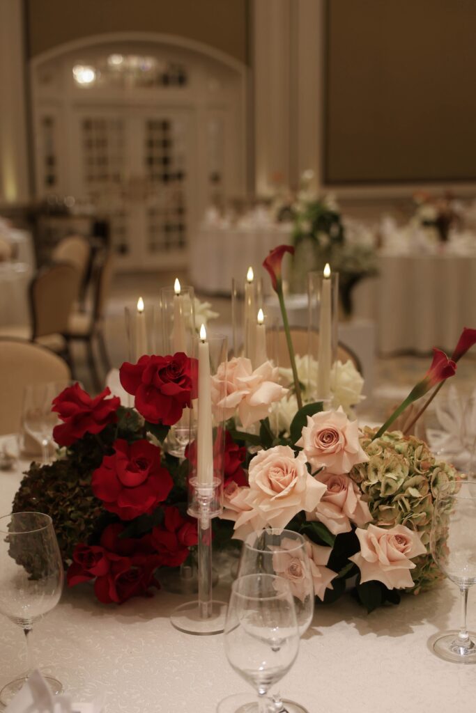 Romantic reception table styling with elevated floral centrepiece featuring blush roses, burgundy blooms, candlelight, and refined modern classic design at Raffles Hotel Singapore