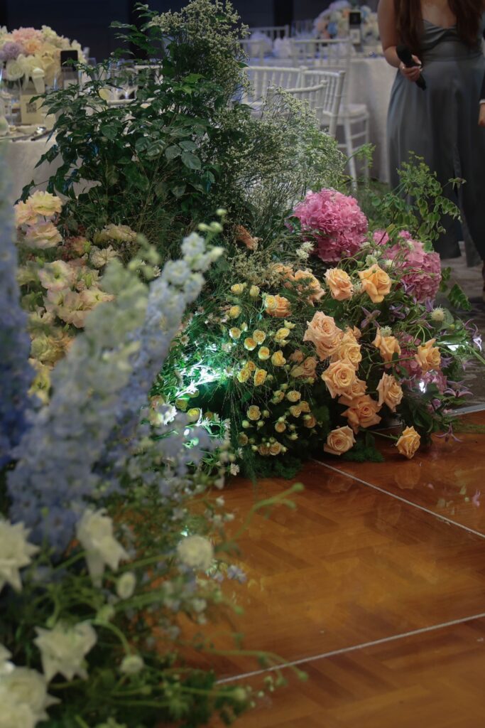 Close-up of lush floral cluster with hydrangeas, roses, delphiniums, and soft foliage in a natural garden-inspired arrangement framing the dance floor at The Outpost Hotel