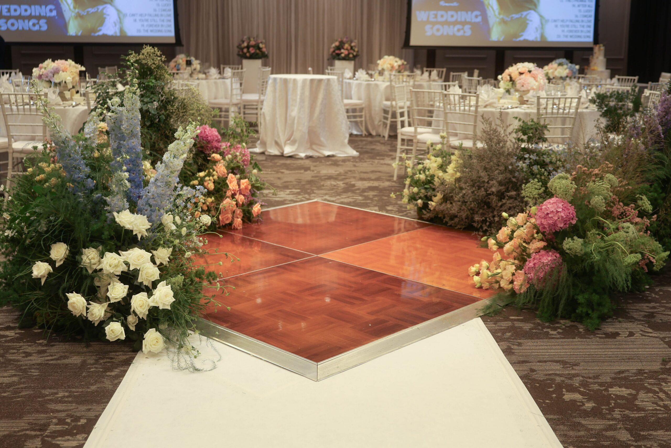Blue and pink floral arrangements with hydrangeas, delphiniums, roses, and soft garden-style clusters framing a central dance floor in a romantic, airy style at The Outpost Hotel