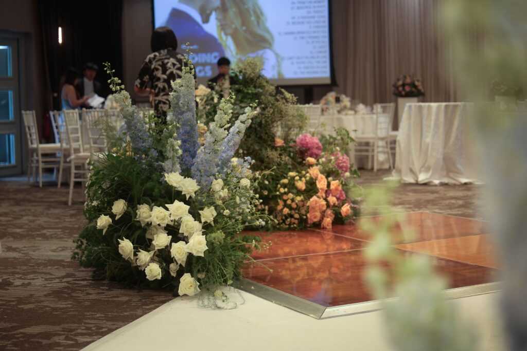 Blue and blush floral clusters with hydrangeas, delphiniums, roses, and soft foliage framing the dance floor entrance in a light, romantic garden style at The Outpost Hotel