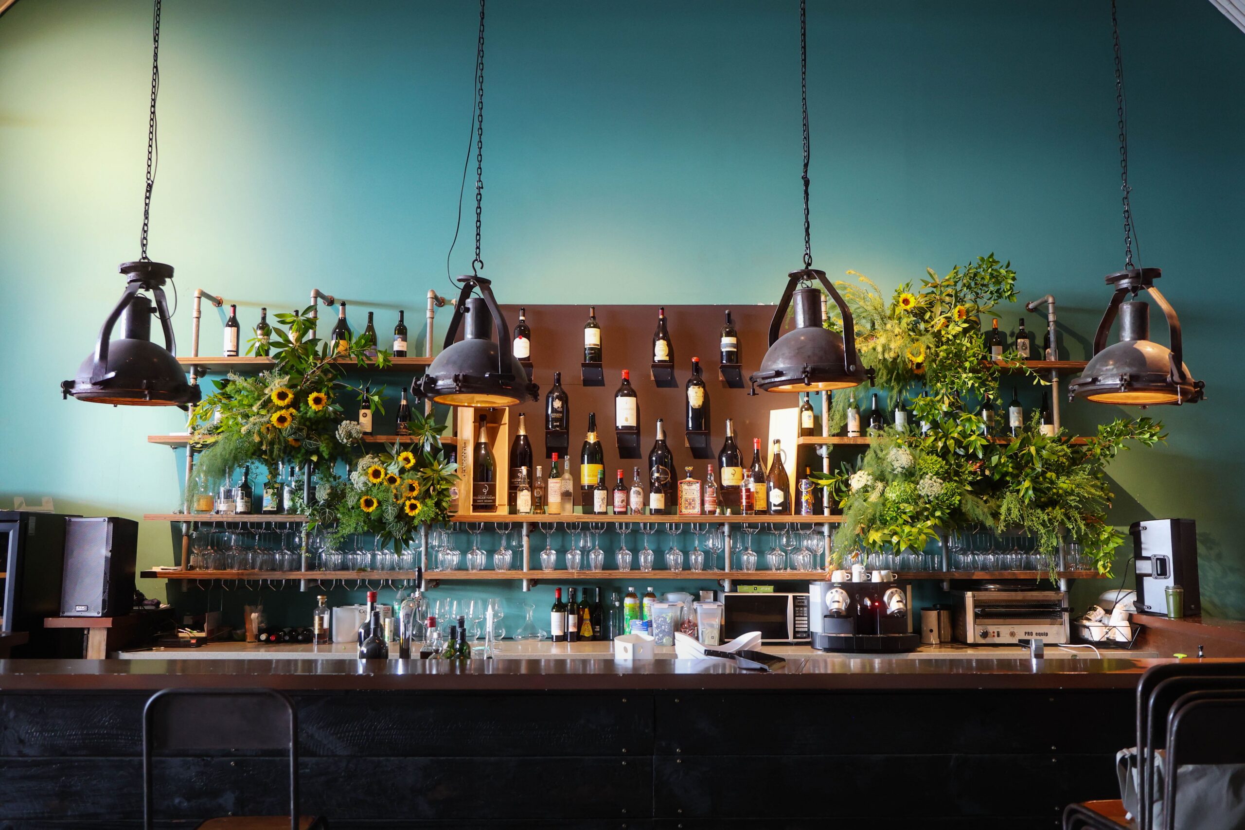 Organic floral installation behind the table bar featuring sunflowers, lush textured greenery, cascading foliage, and natural rustic styling at Cargo39, Singapore.