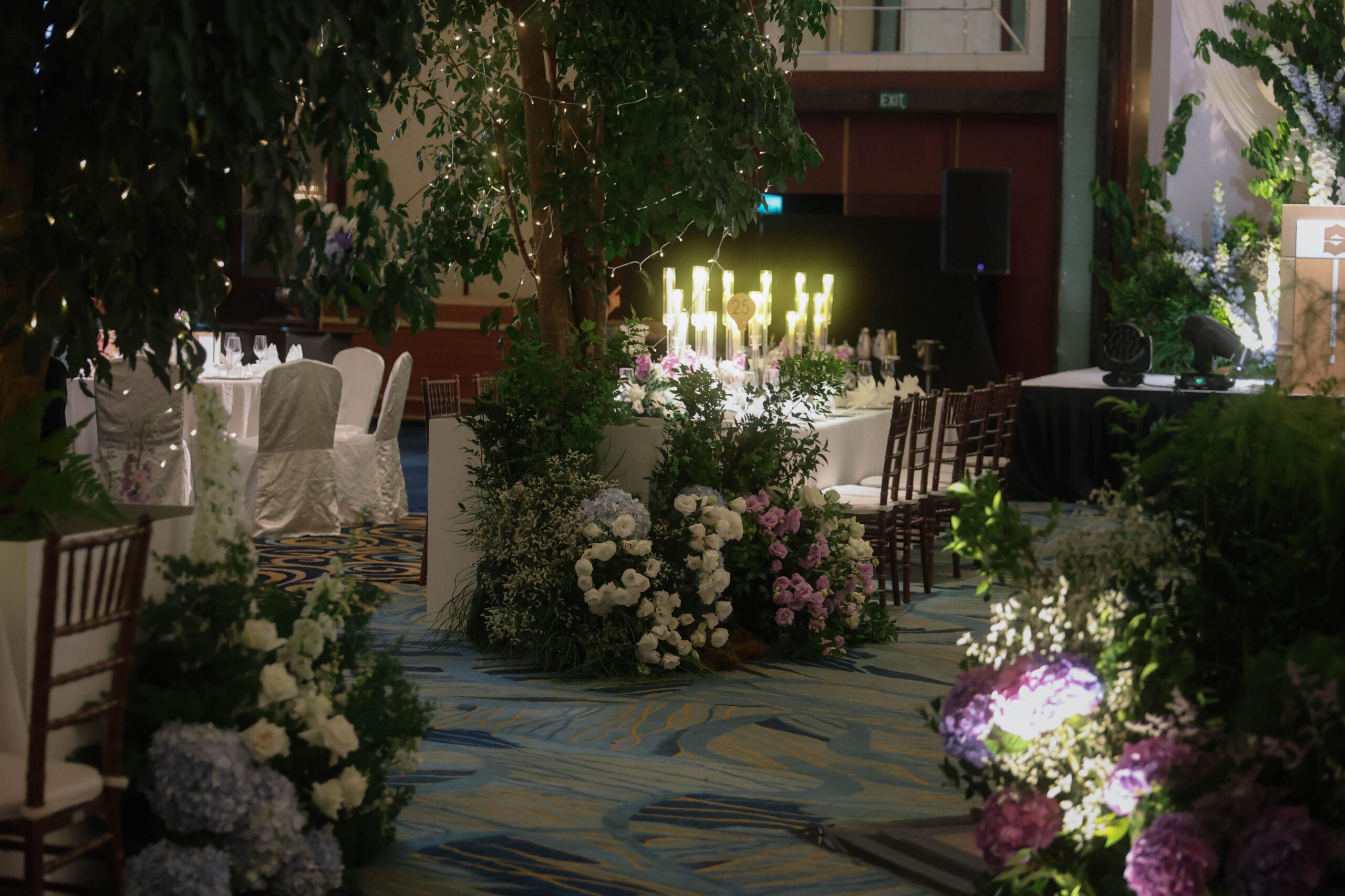 Immersive ballroom forest wedding styling with towering trees, candlelight, and pastel floral arrangements at Shangri-La Singapore