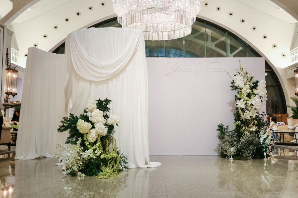 Wide wedding ceremony setup featuring white and green floral installations framing a structured privacy wall design, The Clifford Pier Singapore