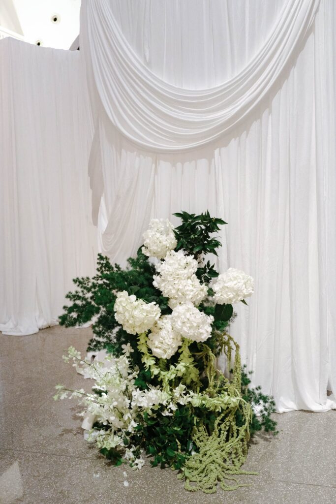 White and green floral cluster styled under soft drapery creating a gentle wedding corner installation, The Clifford Pier Singapore