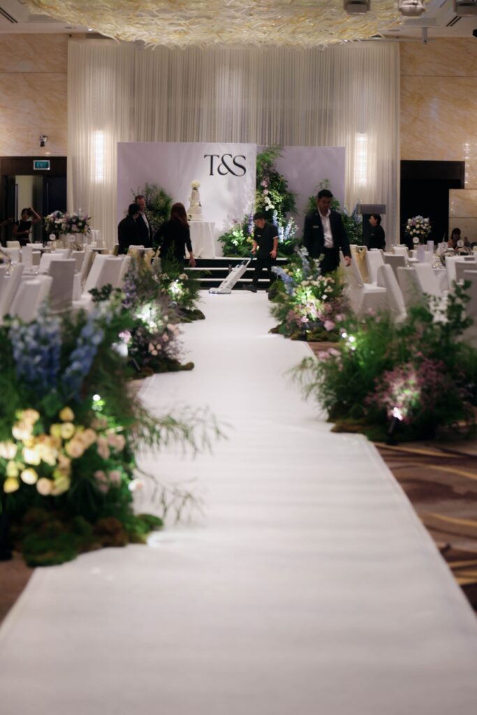 Wide view of a nature-inspired ballroom wedding aisle lined with organic wildflower arrangements, moss, rocks, and layered floral styling leading towards the stage at Westin Singapore.