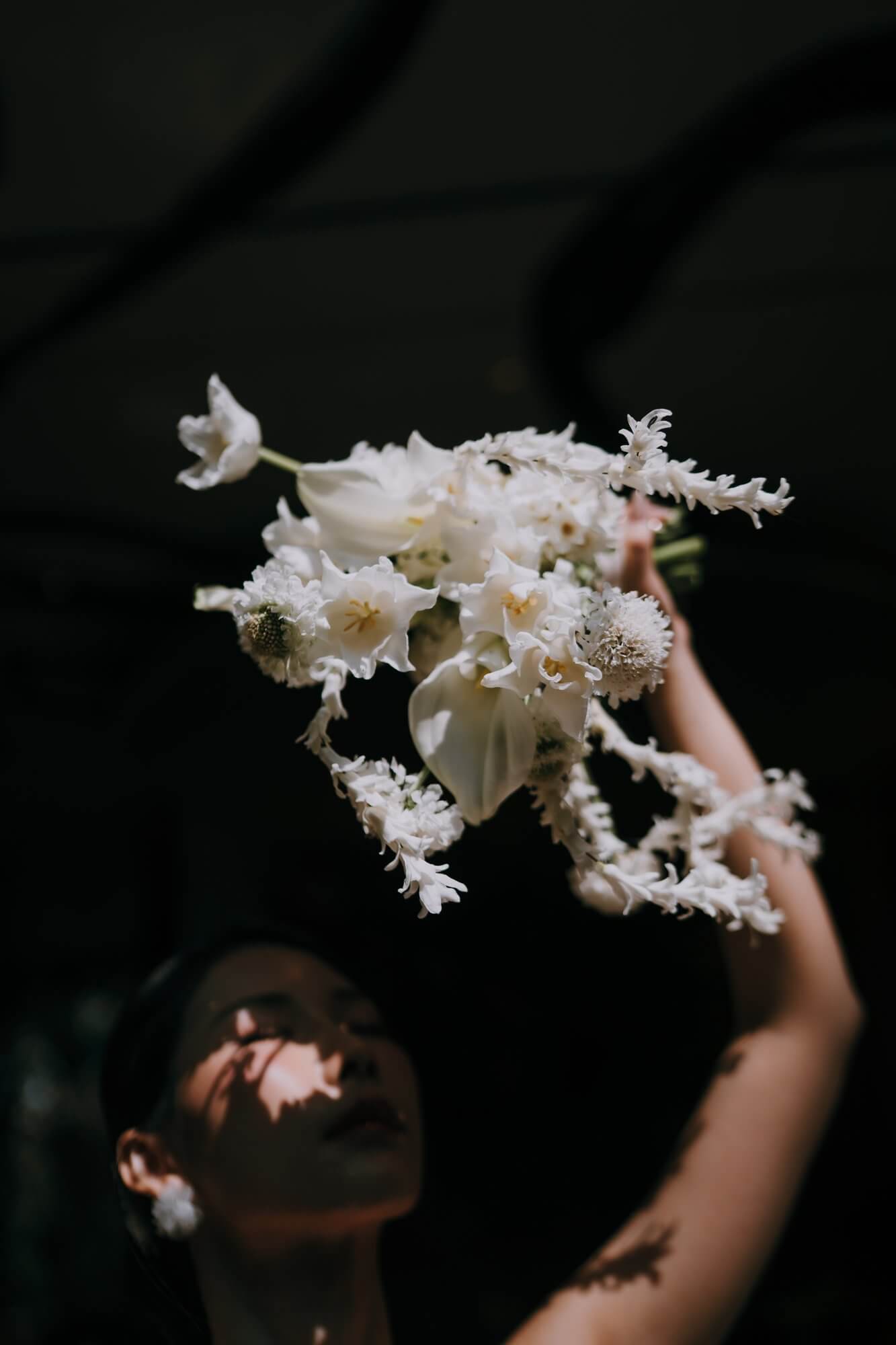 All-white bridal bouquet of calla lilies, tulips and cascading blooms held up in dramatic light