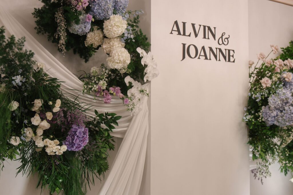 Wedding sign feature styled with gathered drapery, hydrangeas, white roses, and lush garden-inspired florals at Shangri-La Singapore