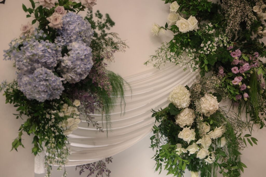 Close-up hydrangea floral styling with white roses, soft blue blooms, and textured greenery against draped wedding backdrop at Shangri-La Singapore
