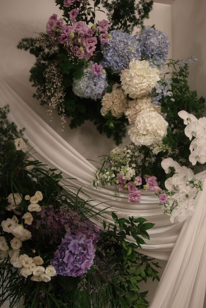 Pastel blue and purple hydrangea floral clusters with flowing drapery and layered greenery in romantic ballroom styling at Shangri-La Singapore