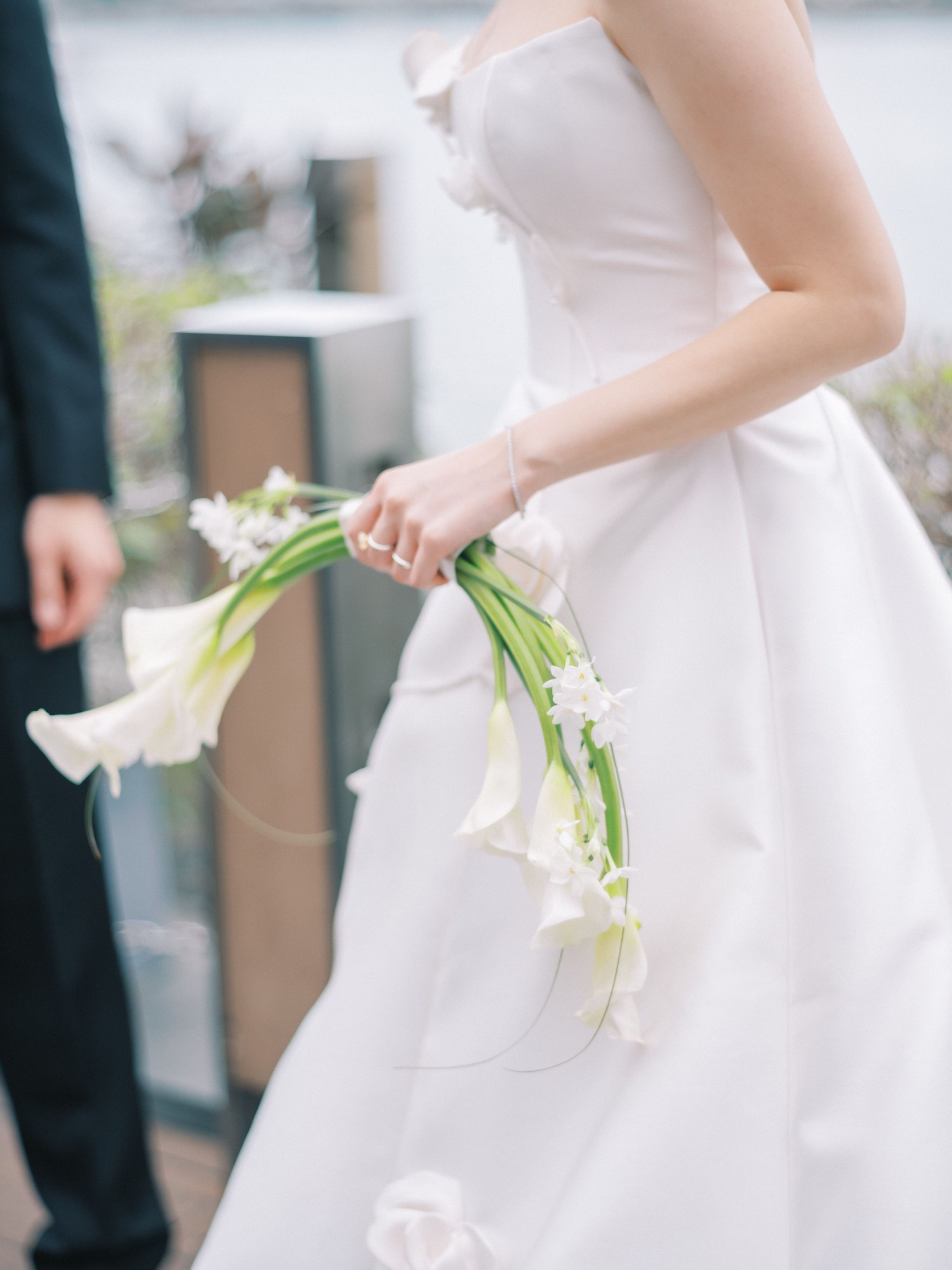 Calla lily wedding bouquet in a white crescent, held by a bride in a white gown