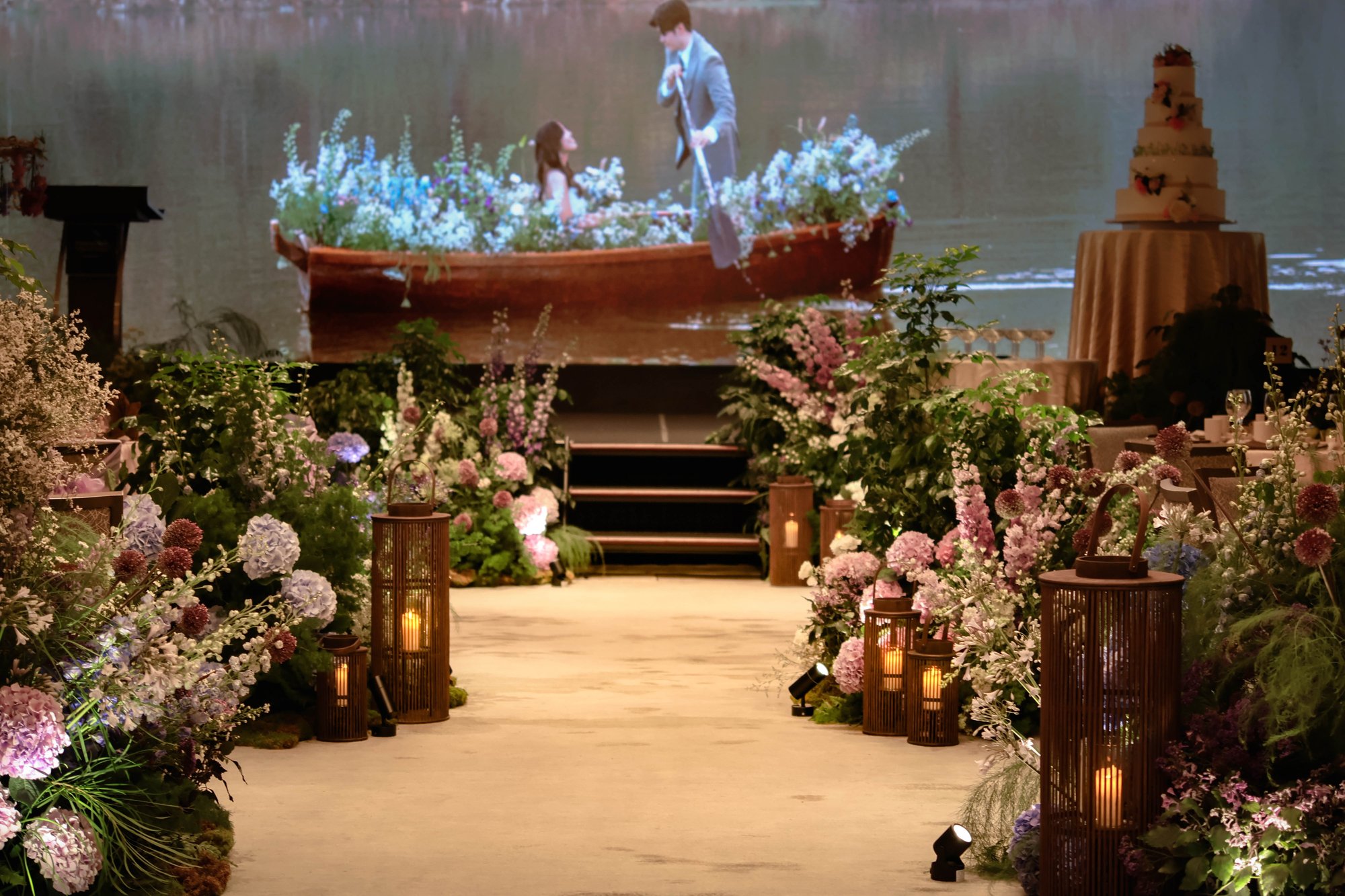 flower-filled rowboat projection above a lantern-lined aisle of hydrangea and delphinium
