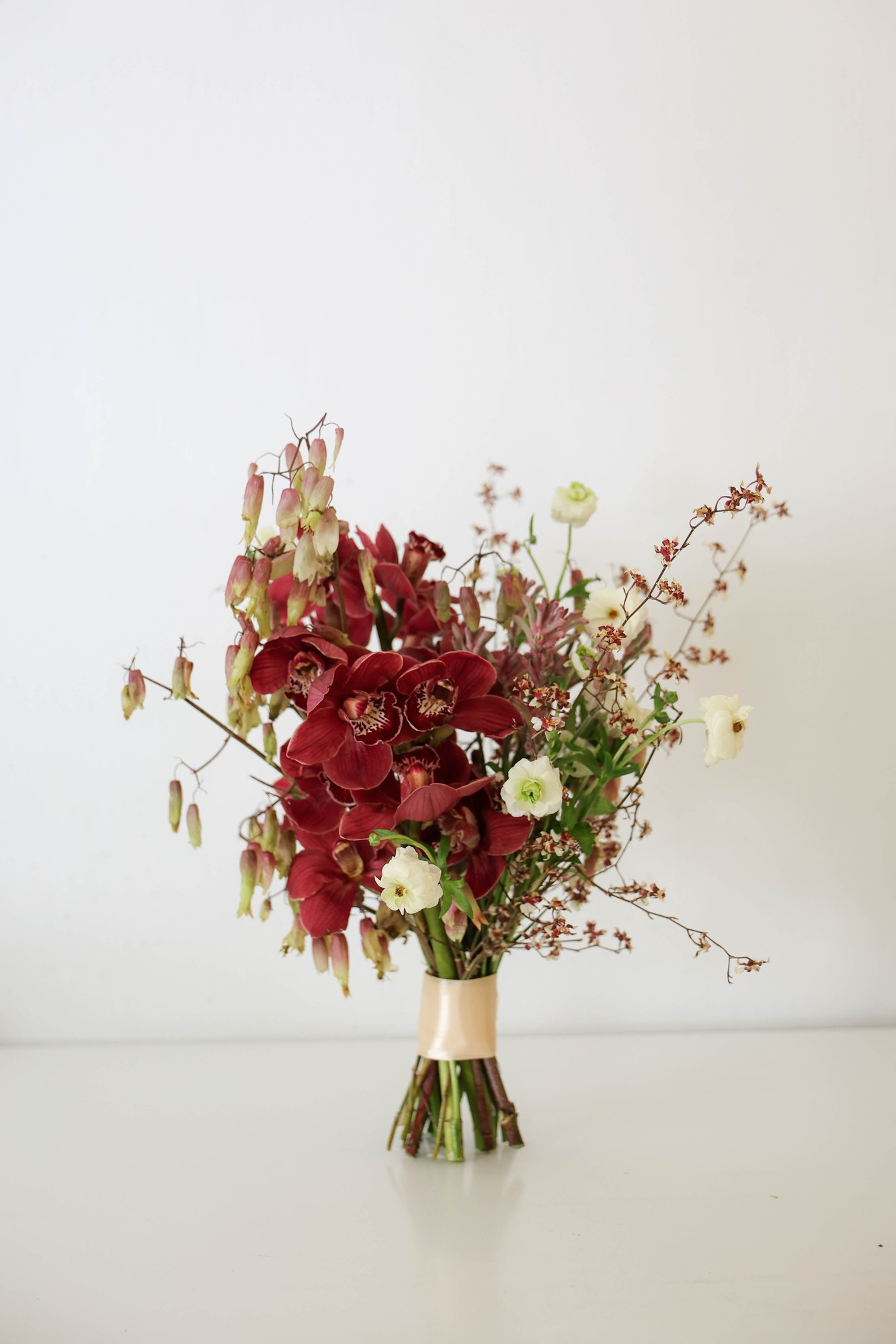 Maroon orchid bouquet of deep burgundy orchids, white ranunculus and kangaroo paw on airy branches