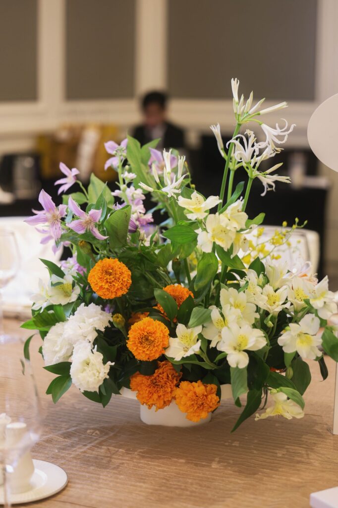 St Regis marigold wedding centrepiece of marigold, purple clematis and white blooms in a footed bowl