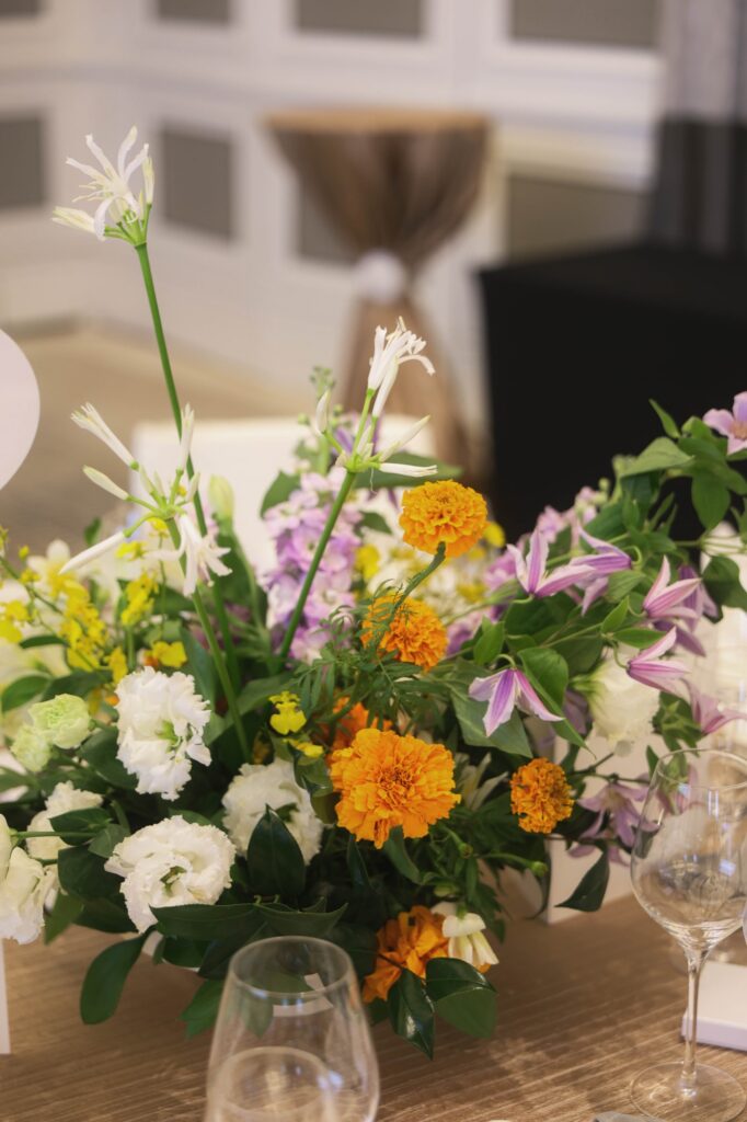 Marigold centrepiece at a St Regis wedding with clematis, white blooms and oncidium beside a wine glass