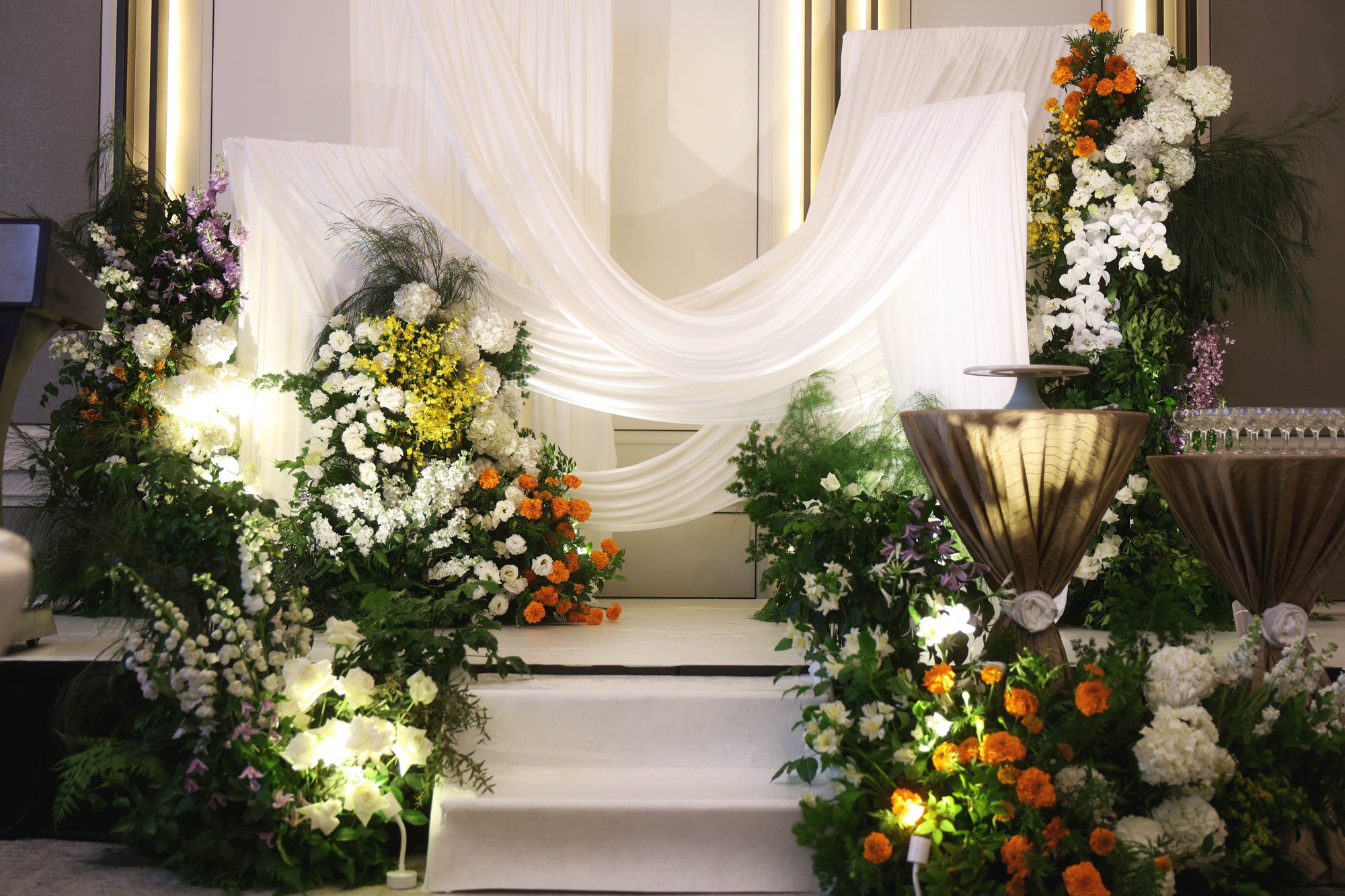 St Regis marigold wedding stage backdrop of white drapery and gold arches with marigold and white florals