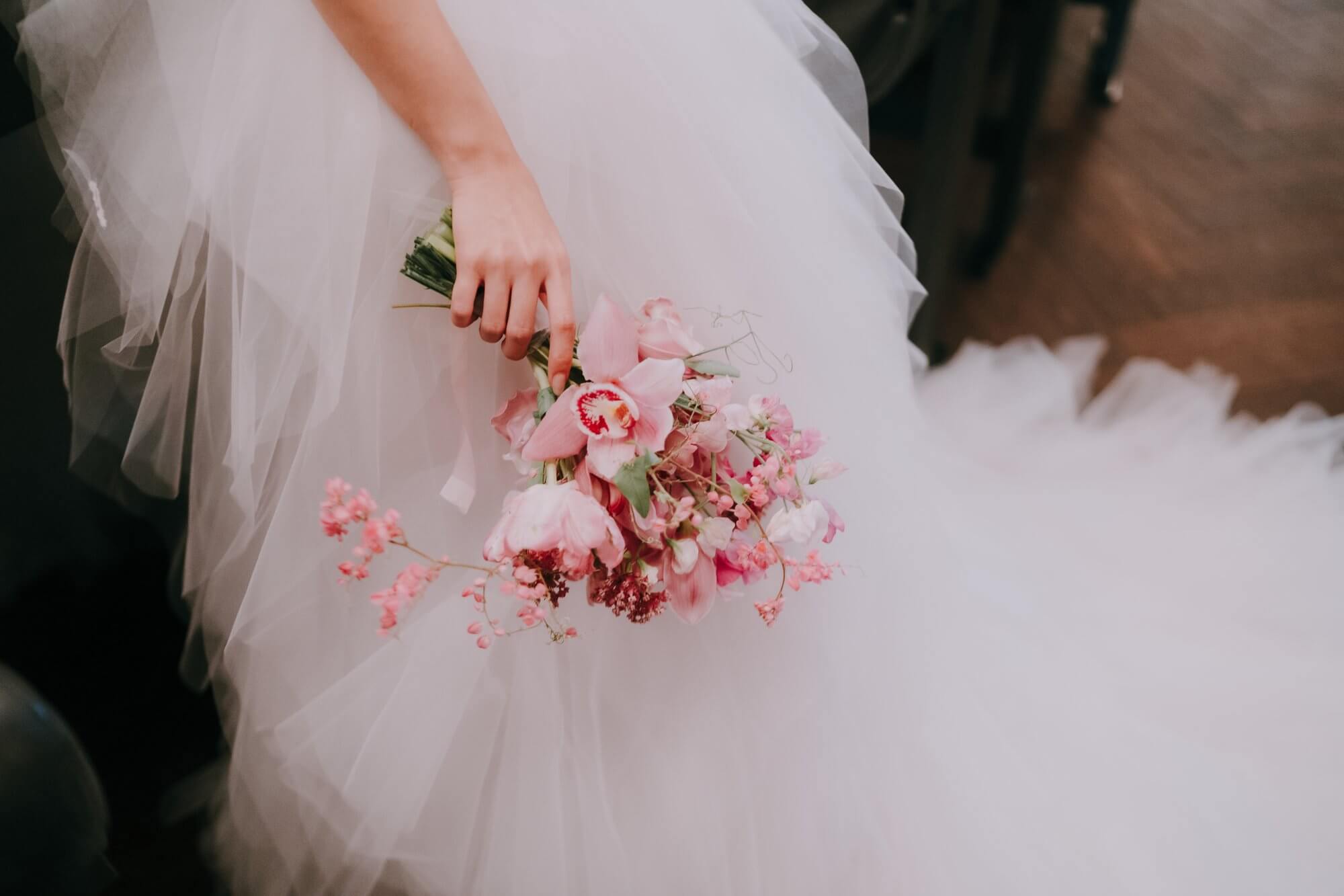 Pink bridal bouquet of cymbidium orchids, sweet peas and coral vine held against a tulle gown