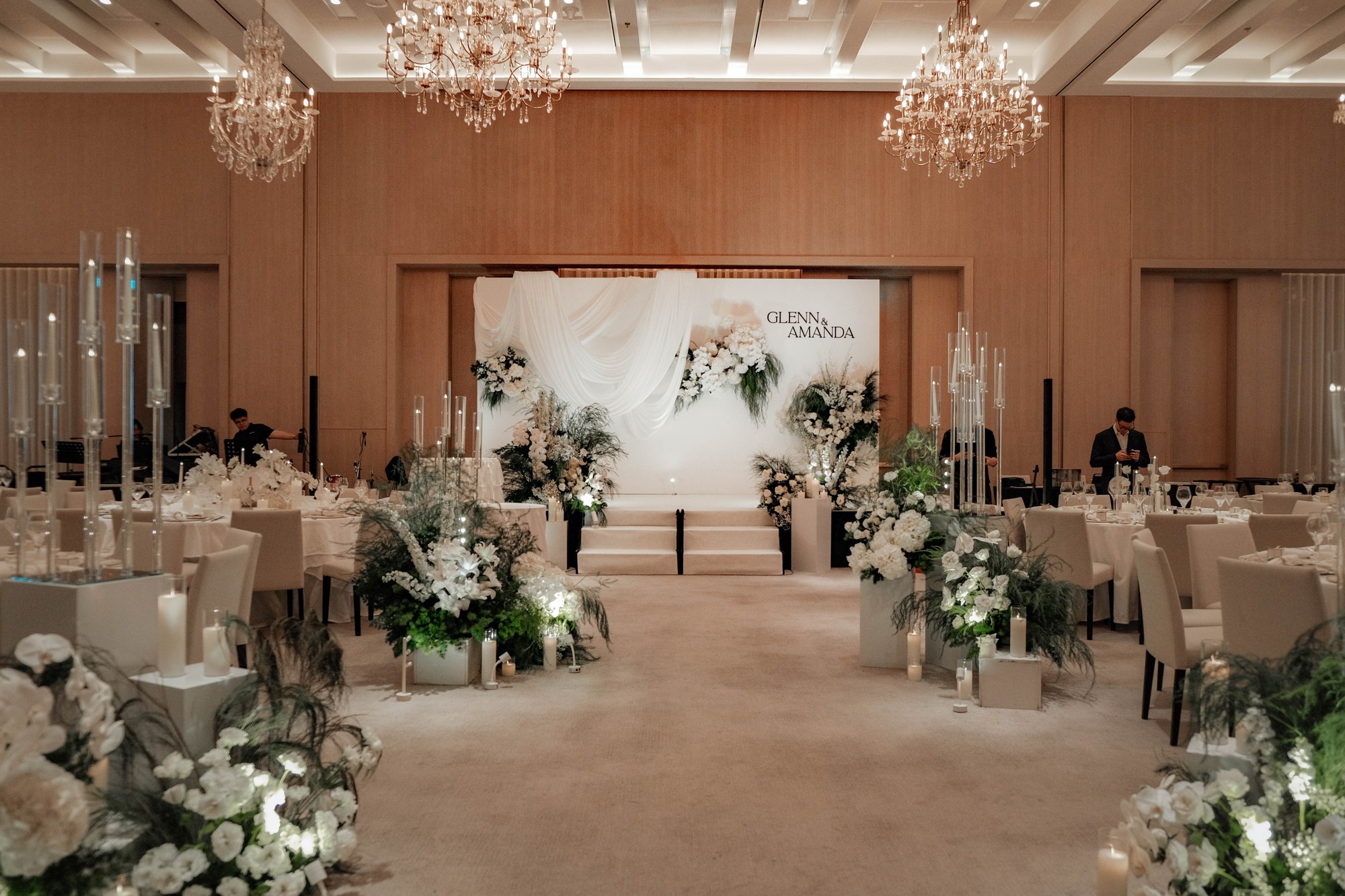 Edition Hotel ballroom under crystal chandeliers, white aisle arrangements leading to the grand backdrop